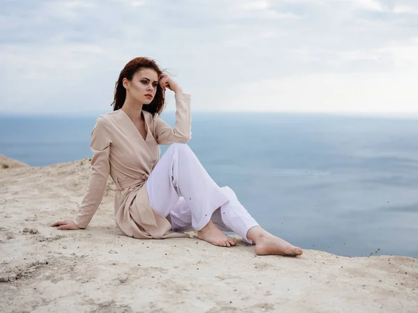 Une femme en vêtements légers est assise sur un rocher avec l'océan en arrière-plan — Photo