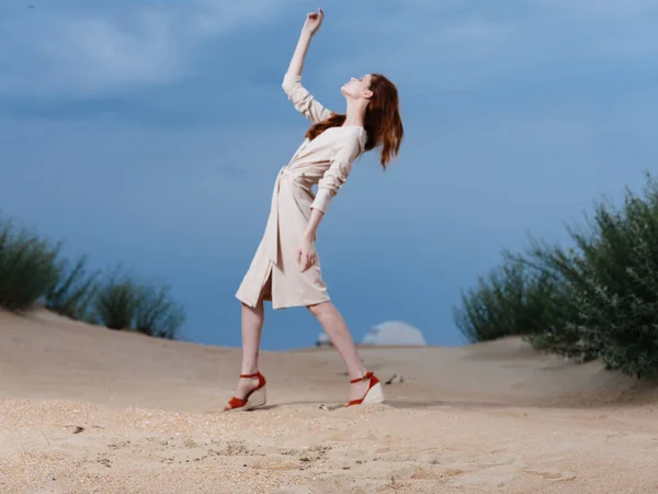 Een vrouw in een zonnejurk loopt over het zand op het strand en struiken op de achtergrond — Stockfoto