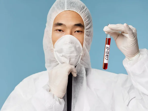Людина азіатського походження захищає одяг лабораторні аналізи крові на синьому фоні — стокове фото