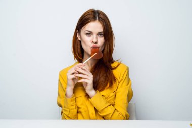 Kalp şeklinde lolipopu olan neşeli çekici kadın masada oturuyor.