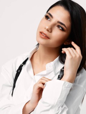 Askılı beyaz gömlekli tatlı esmer, elleriyle saçına dokunuyor.