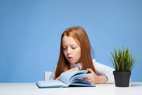 テーブルスクールで宿題をする女の子青の背景 — ストック写真