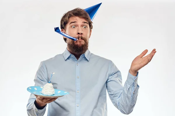 Muž slaví narozeniny na světlém pozadí s dort v talíř flétna zábavná čepice — Stock fotografie