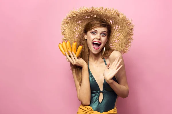 Mulher na praia chapéu de palha bananas segurando frutas Fato de banho exótico fundo rosa — Fotografia de Stock