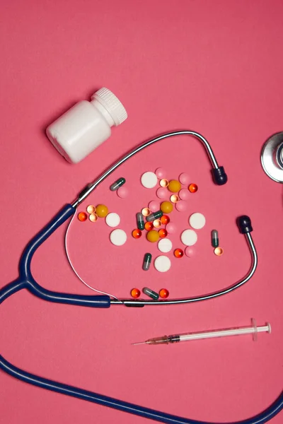 丸薬白い瓶聴診器健康注射器ピンクの背景クロップビュー — ストック写真