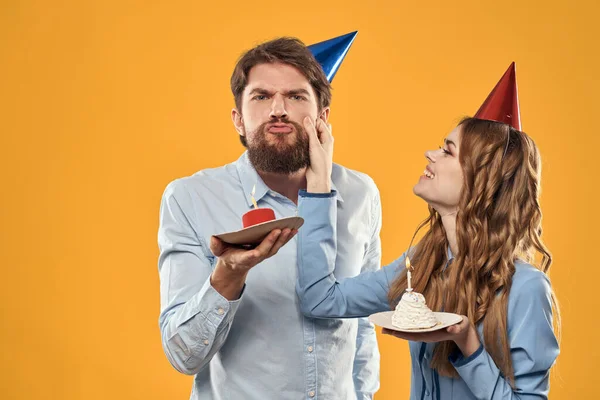 Birthday party man and woman in a cap with a cake on a yellow background cropped view — Stock Photo, Image