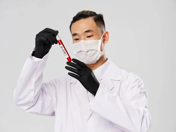 Man of Asian appearance black gloves blood test diagnostics research laboratory gray background — стокове фото
