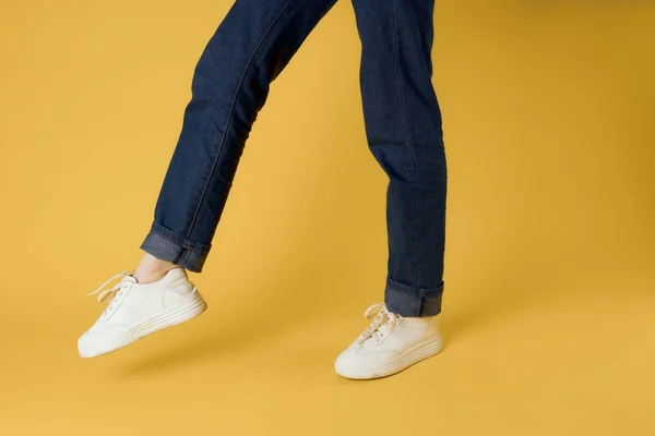 Piede gesto bianco scarpe da ginnastica moda jeans street style giallo sfondo — Foto Stock