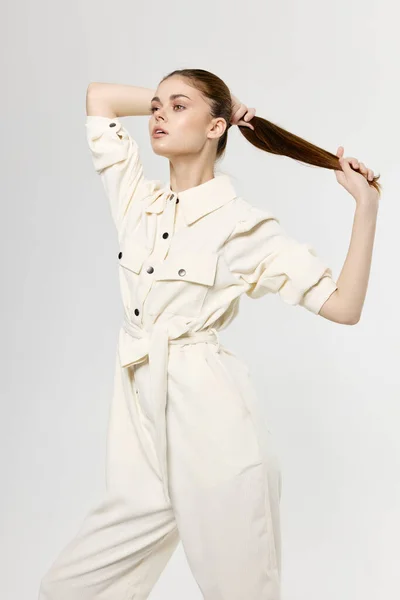 Woman in white jumpsuit touches hair on her head with her hands on a light background — Stockfoto