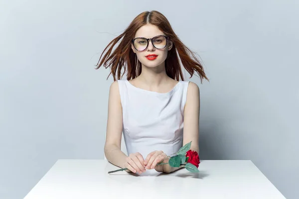Roztomilá zrzavá žena sedící u stolu s růžovým květem v ruce okouzlující model — Stock fotografie