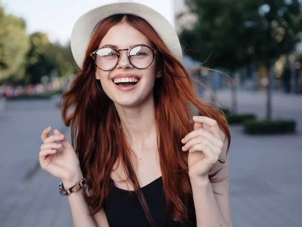 Рыжая женщина в белой шляпе и очках ходит по улице летом — стоковое фото