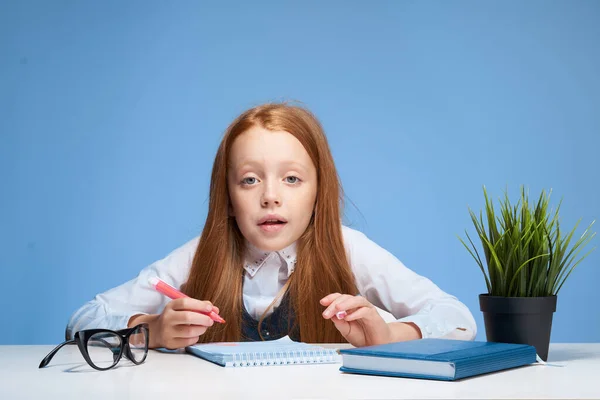 教科書のあるテーブルに座っている赤髪の女の子子供の頃 — ストック写真