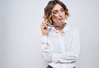 Hafif arka planda bir kadın ellerinde gözlük ve beyaz bir gömlek tutuyor.