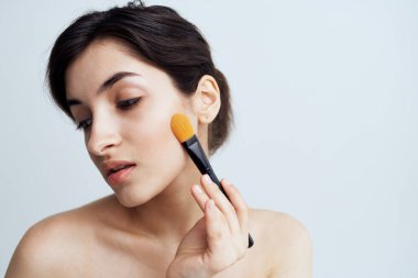 Güzel esmer, çıplak omuzlu. Çekici görünmek için yüzüne makyaj yapıyor.