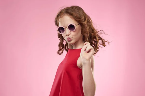 戴着卷发太阳镜的女孩童年时代欢乐的粉色背景 — 图库照片