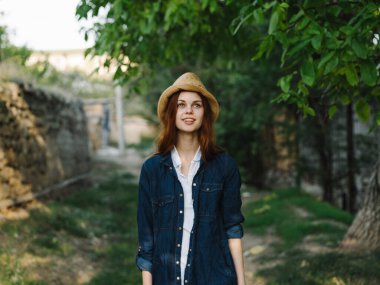 Şapkalı ve kot ceketli bir kadın kırsal alanda duygular yaratıyor.