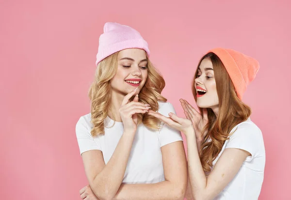 Две девушки в разноцветных кепках обнимает гламурный розовый фон — стоковое фото