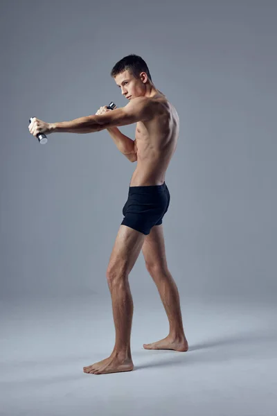 Sportowy mężczyzna w czarnych spodenkach z hantlami w dłoniach stwarzający motywację fitness — Zdjęcie stockowe