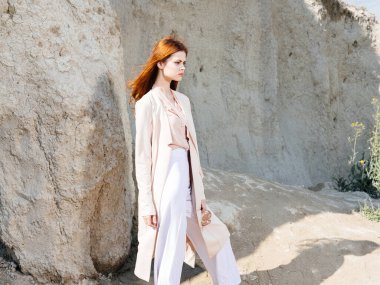 Pantolon ve süveter giymiş bir kadın ve büyük kayaların yanında.