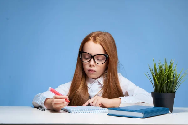 テーブルスクールで宿題をしている眼鏡をかけた赤い髪の少女 — ストック写真