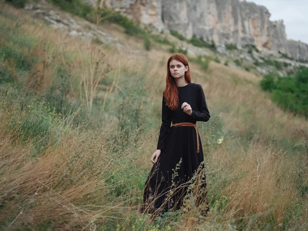 Viajante na floresta em um prado nas montanhas vestido preto cabelo vermelho — Fotografia de Stock