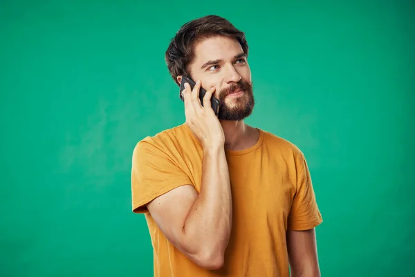 Hombre con teléfono móvil y camiseta amarilla sobre fondo verde vista recortada — Foto de Stock