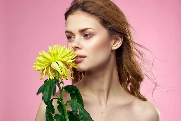 Hermosa chica con una flor amarilla sobre un fondo rosa maquillaje hombros desnudos — Foto de Stock