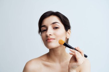 Güzel esmer, çıplak omuzlu. Çekici görünmek için yüzüne makyaj yapıyor.