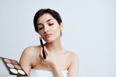 Çıplak omuzlu bir kadın makyaj malzemesi kullanıyor.