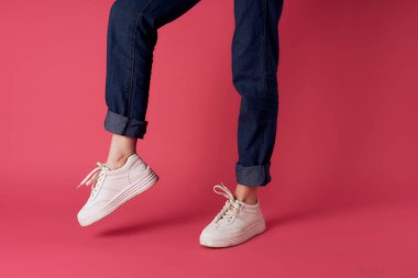 Kadın ayakları, beyaz spor ayakkabıları, sokak moda, pembe arka plan.