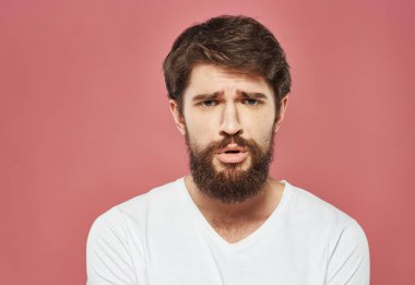 Pembe arka planda beyaz tişörtlü üzgün bir adamın portresi.