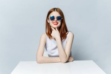 Gözlüklü kadın beyaz bir masada oturuyor. Duygular çekici görünüyor.