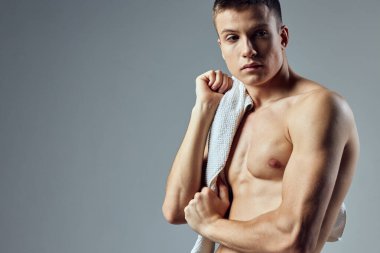 Omuzlarında havlu olan sportif adam, arka planda gri bir görünüm bıraktı.