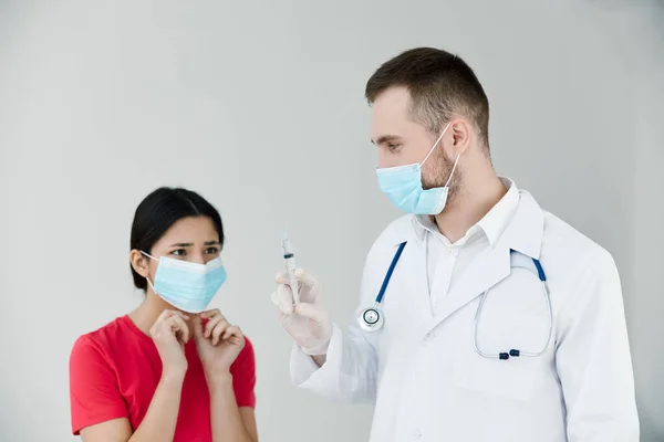 医療用マスクの女性患者は医者の手に注射器を見ます — ストック写真