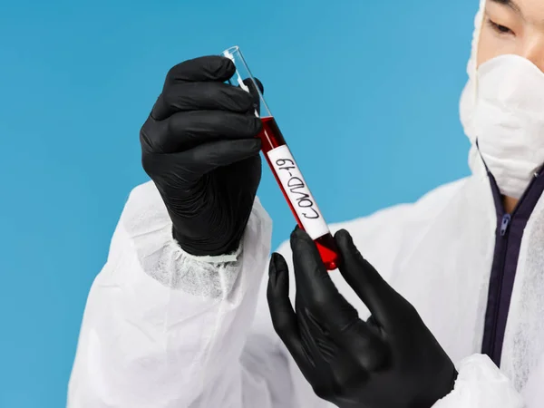 Чоловік тримає аналіз крові на ковадлі-19 в руках чорні захисні рукавички синій фон — стокове фото