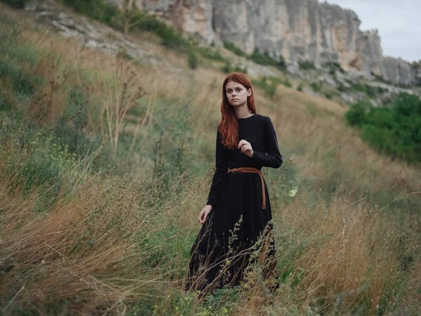 Viajante na floresta em um prado nas montanhas vestido preto cabelo vermelho — Fotografia de Stock