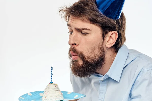 케이크 접시를 들고 밝은 배경 배경에 파란 셔츠를 입은 남자 생일 파티 모자를 쓴 남자 — 스톡 사진