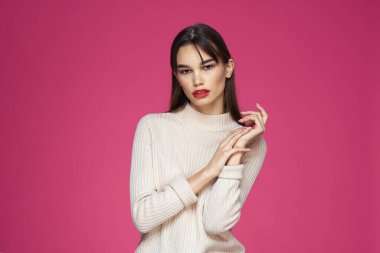 Uzun saçlı, kırmızı dudaklı beyaz bluzlu, pembe arka planlı çekici bir kadın.