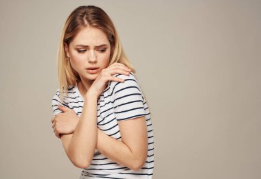 Çizgili tişörtlü bir kadın bej arka planda kendine sarılıyor.