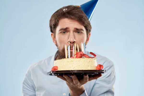 Hombre barbudo con un plato de pastel sobre un fondo azul y un sombrero de fiesta de cumpleaños en su cabeza — Foto de Stock