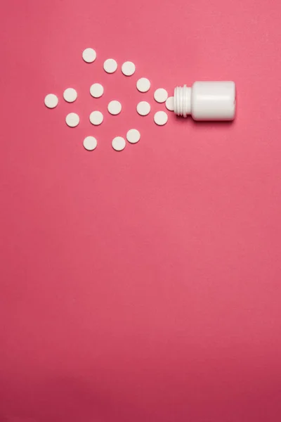 Λευκά χάπια σκορπισμένα σε ροζ φόντο και ένα βάζο με καπάκι πάνω όψη — Φωτογραφία Αρχείου