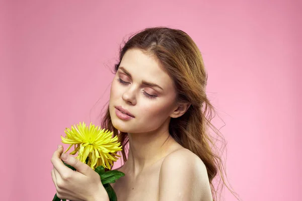 Menina bonita com uma flor amarela em um fundo rosa nua ombros maquiagem — Fotografia de Stock