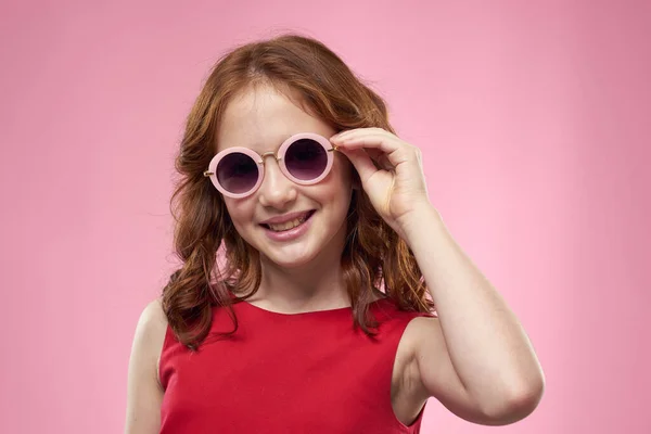 Wesoły mała dziewczynka dzieciństwo ciemne okulary czerwony sukienka styl życia różowy tło — Zdjęcie stockowe