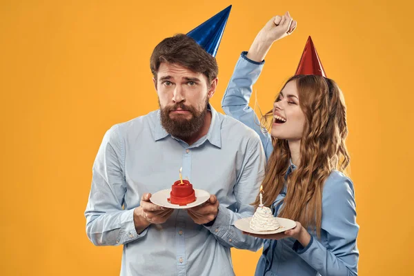 Aniversário festa homem e mulher em um boné com um bolo em um fundo amarelo vista cortada — Fotografia de Stock