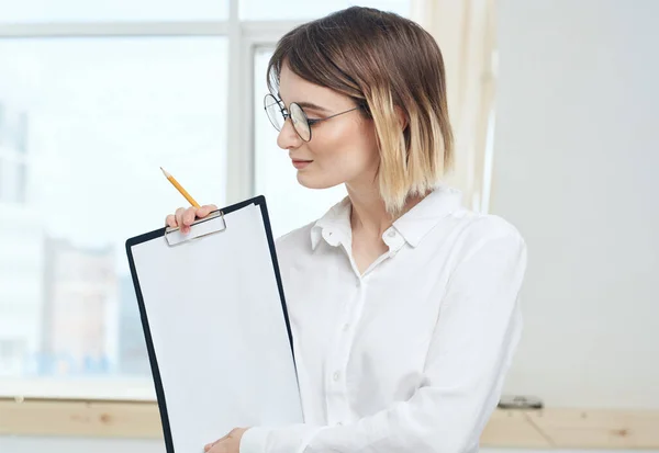 Eine Frau hält einen Ordner mit einem weißen Blatt Papier und einem Fenster im Hintergrund — Stockfoto