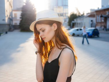 Siyah elbiseli ve beyaz şapkalı bir kadın portresi. Gün batımında binanın yanındaki sokakta.