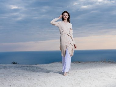 Bir kadın bütün kıyafetlerini dağlarda, deniz kenarında yürür.