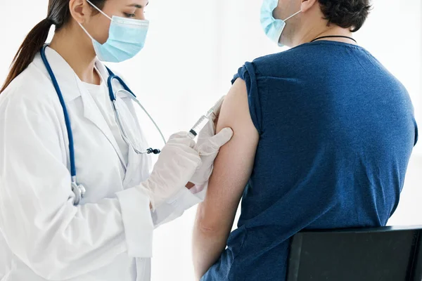 Kvinnlig sjuksköterska i en medicinsk mask injicerar ett vaccin i axeln på en manlig patient — Stockfoto