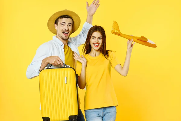 Elinde bavulu olan bir adam ve oyuncak uçağı olan bir kadın sarı arka planda geziye çıkıyorlar. — Stok fotoğraf