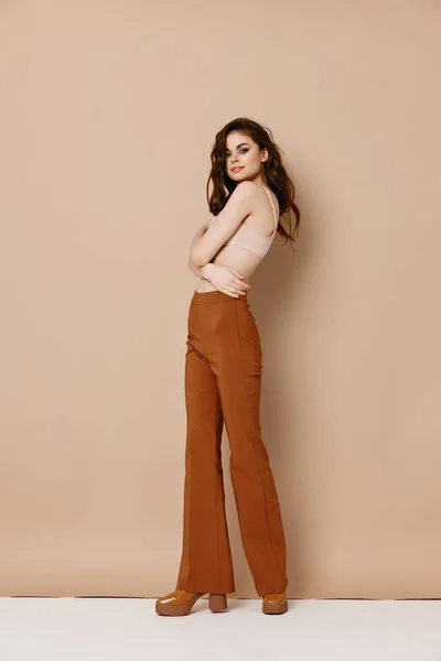 A slender woman in brown trousers and a t-shirt on a beige background — Stock Photo, Image